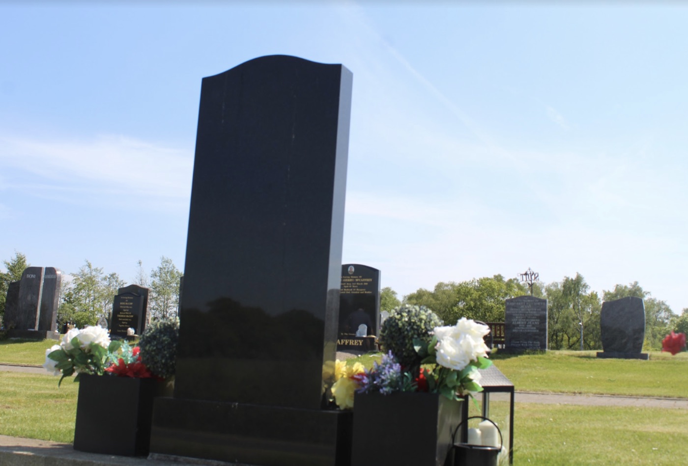 Polished black granite headstone standing in a lawn cemetery