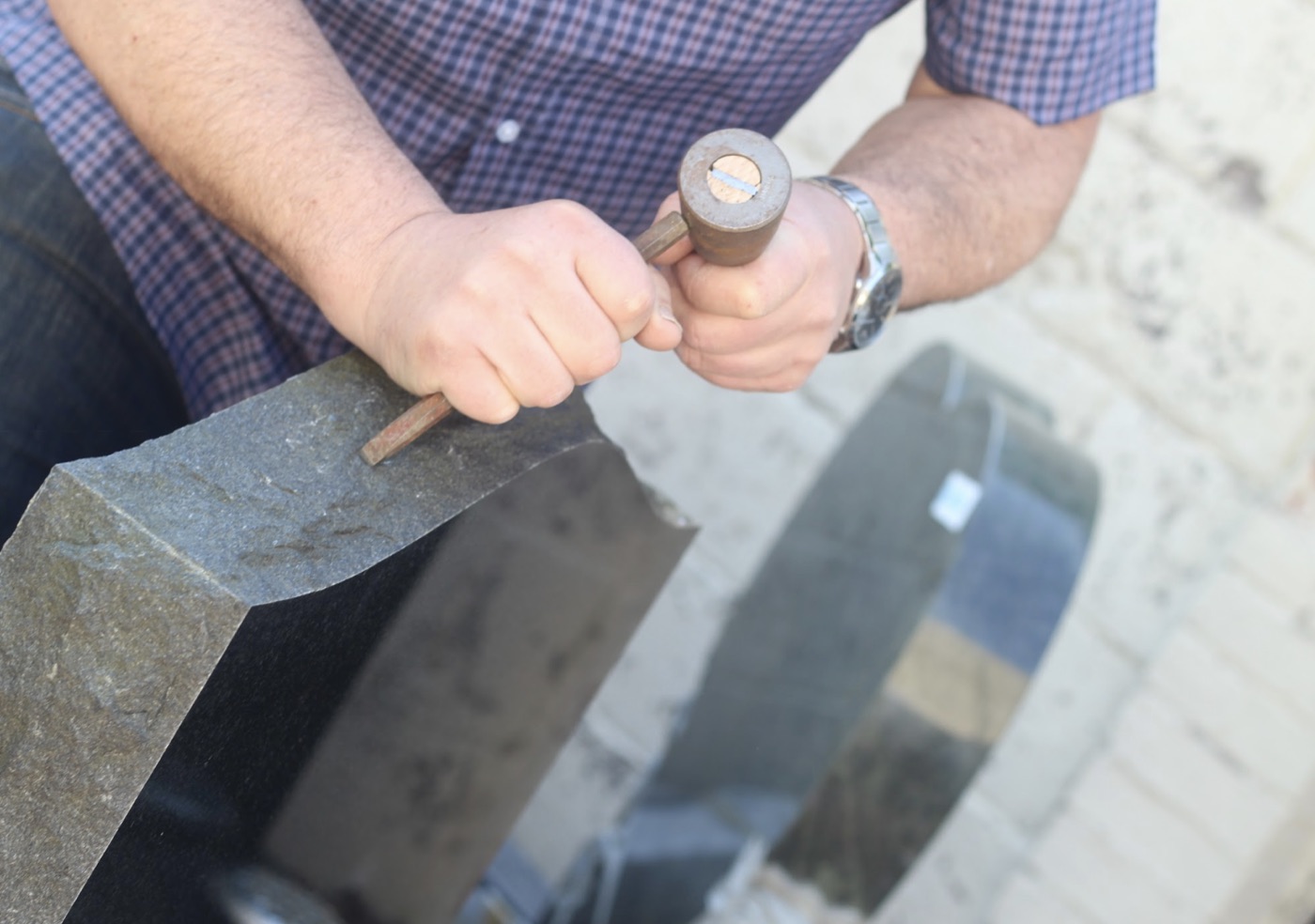 Mason pitching the edge of a granite headstone with hammer and chisel