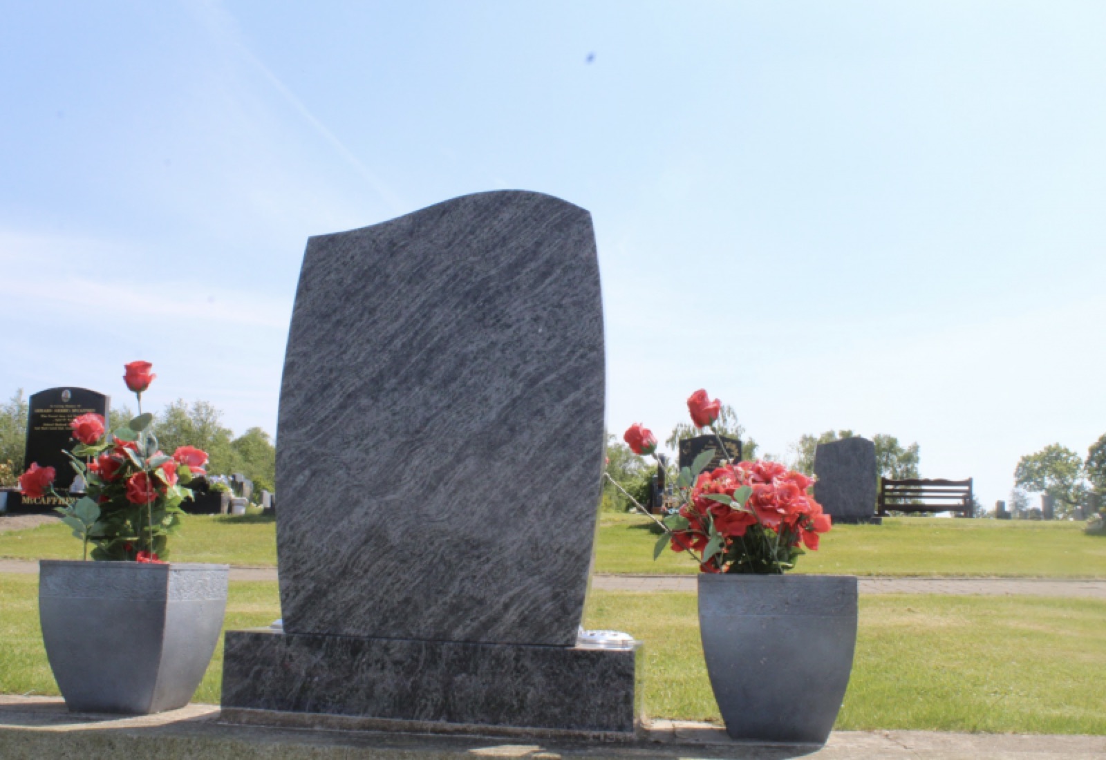 Vizor blue granite headstone with flower vases at a Glasgow cemetery in sunshine